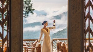 A woman in a white dress standing in a wooden structure with a view of mountains and clouds. - Lannawild Chiang Mai (Mae On)