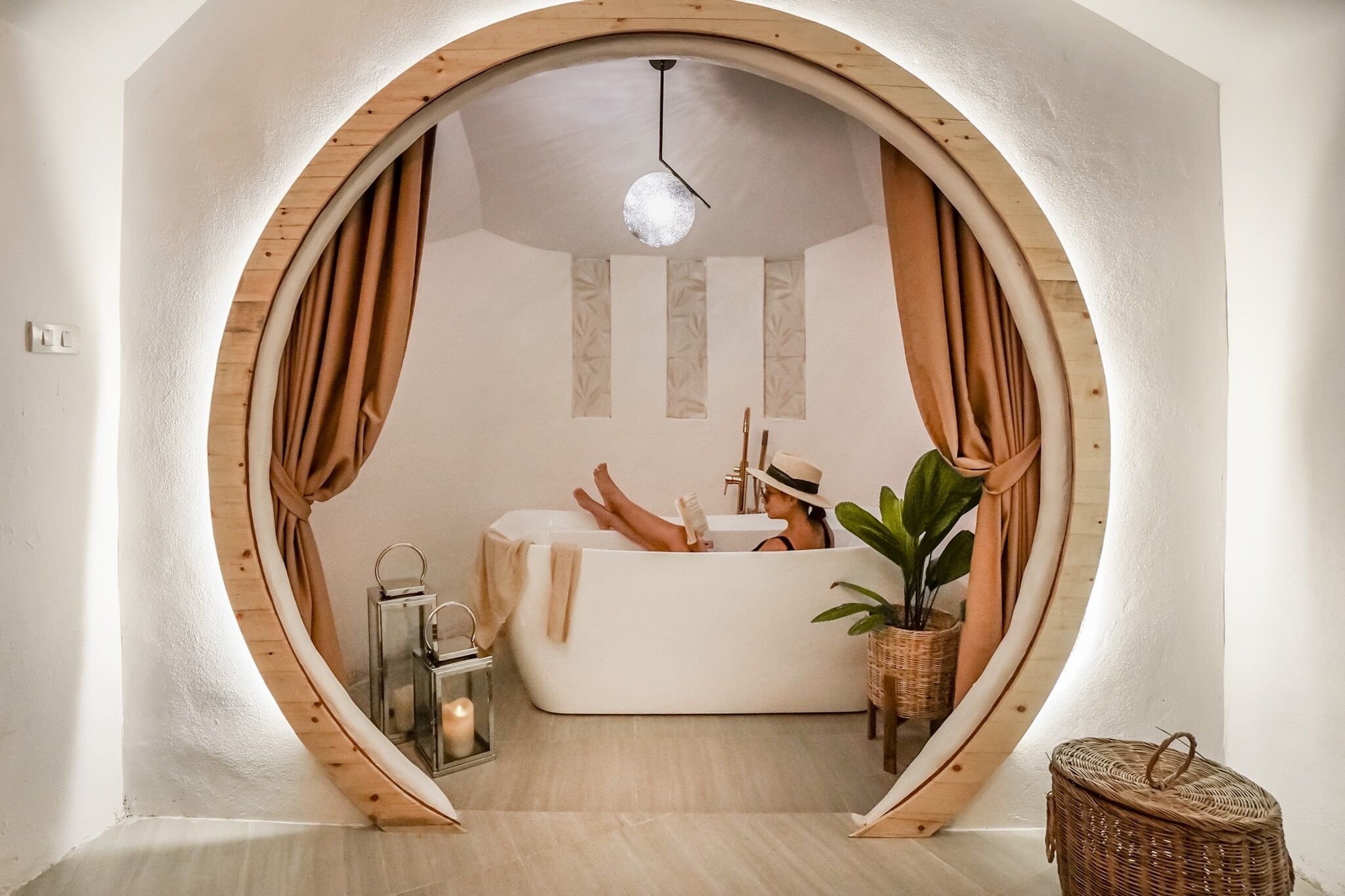 Una habitación circular con una bañera, una lámpara colgante y una planta en maceta.