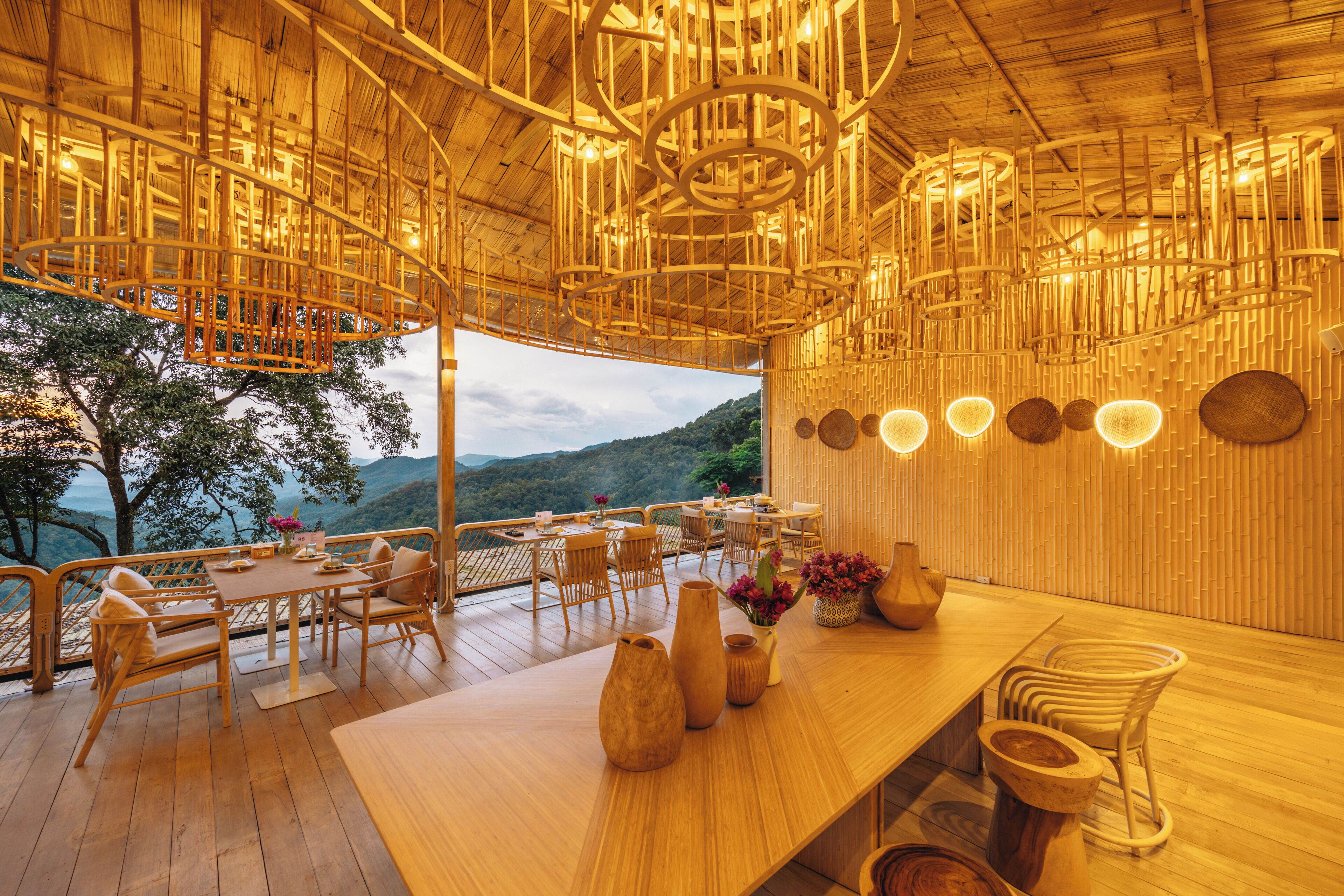 A wooden interior with tables and chairs, a wooden ceiling with hanging light fixtures, and a view of the outdoors.