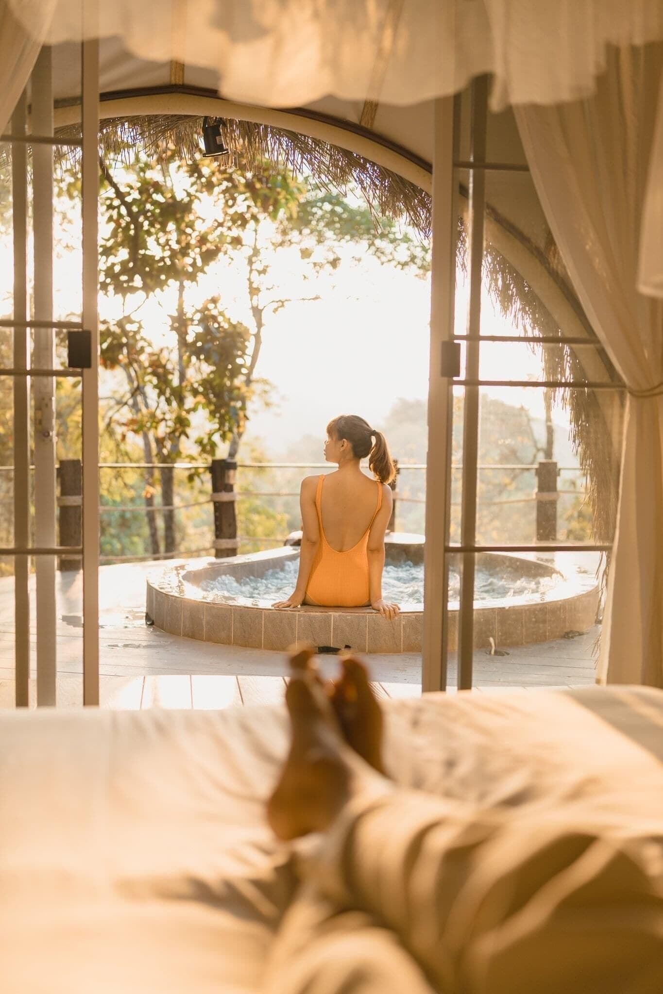 A person sitting in a hot tub with a view of trees and a building in the background.