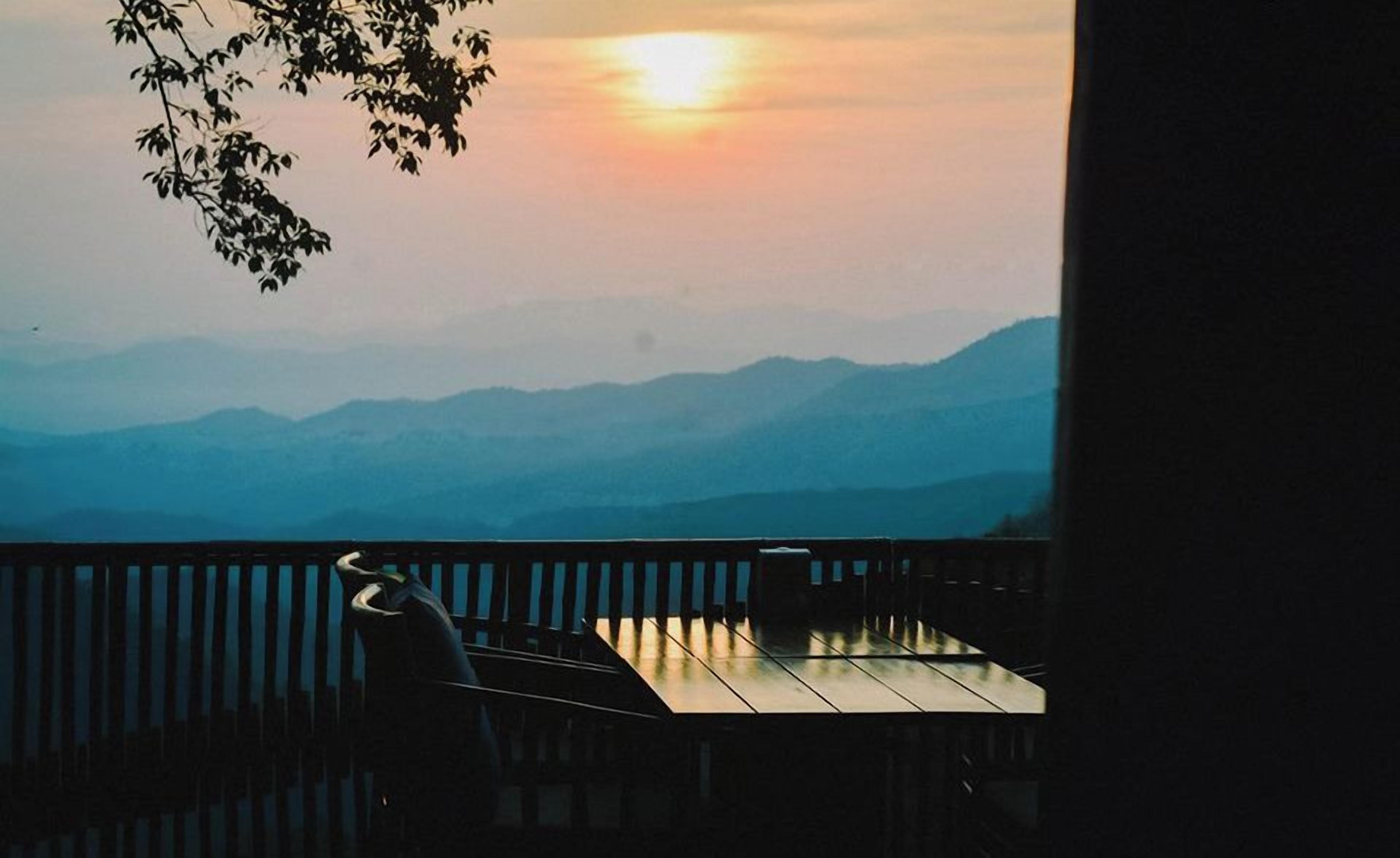 A sunset view from a balcony with a table and chairs.