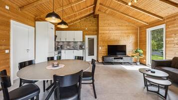 Ein modernes Blockhaus-Interieur mit Essbereich, Küche, Wohnzimmer und einem großen Fenster mit Blick ins Freie.