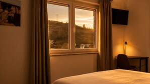 A hotel room with a bed, a desk, a chair, a TV, and a window with curtains. - Luxury Douro Villa with Pool & Panoramic Views (Ferreiros de Avões)