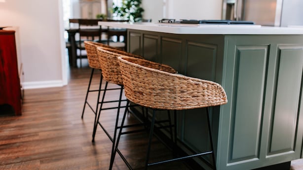 Een keuken met een bar, houten vloeren en groene kastjes.
