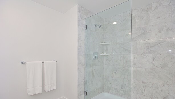 Ein modernes Badezimmer mit einer gläsernen Duschkabine, Marmorwänden und zwei weißen Handtüchern, die an der Wand hängen.