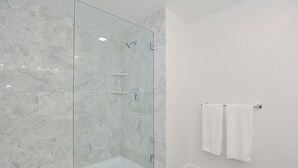 Een moderne badkamer met een douchecabine van glas, witte marmeren tegels en een witte handdoekhouder.