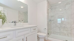 A modern bathroom with a glass-enclosed shower, a white sink, and a large mirror. - Premium Ocean View Condo (1,100S.F.) (Plymouth)