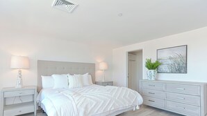 A bedroom with a large bed, two bedside tables, a dresser, and a door leading to another room. - Premium Ocean View Condo (1,100S.F.) (Plymouth)