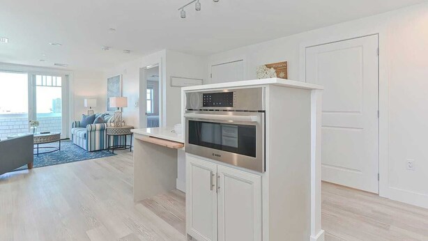A modern kitchen with a built-in oven and microwave, a dining area with a round table, and a living room with a sofa and a lamp.