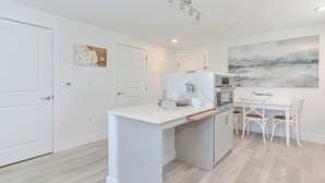A modern kitchen with white cabinetry, a marble countertop, and a dining area with white chairs.