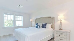 A bedroom with a large bed, two bedside tables, and a window with blinds.