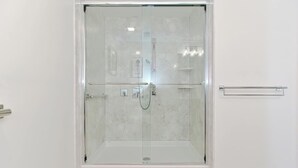 A glass-enclosed shower with a control panel, a towel rack, and a door handle.