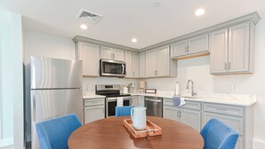 A modern kitchen with light grey cabinets, stainless steel appliances, and a round wooden table with blue chairs.