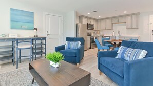 A modern living room with a sofa, armchairs, a coffee table, and a dining area with chairs.