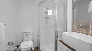 A modern bathroom with a glass-enclosed shower, a white toilet, and a sink with a wooden countertop.