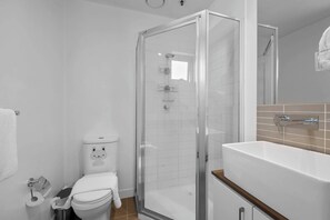 Un baño moderno con ducha de vidrio, inodoro blanco y lavamanos con encimera de madera.