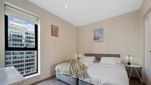 Een hotelkamer met een bed, nachtkastjes, een raam met uitzicht op de stad en een klein bureau.