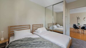 A modern bedroom with two wooden beds, a large mirror, and a desk with chairs.