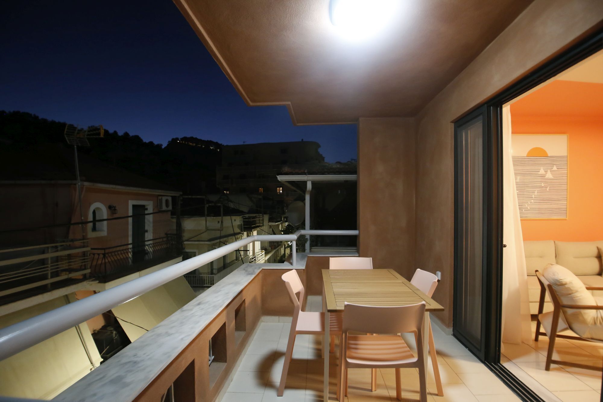 Un balcon avec une table et des chaises, une balustrade et une vue sur les bâtiments et les collines environnants.