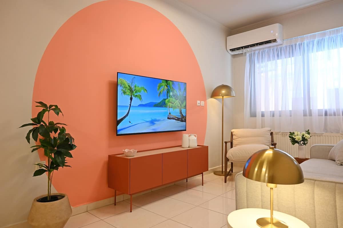 A living room with a TV mounted on a peach-colored wall, a sofa, a floor lamp, and a potted plant.
