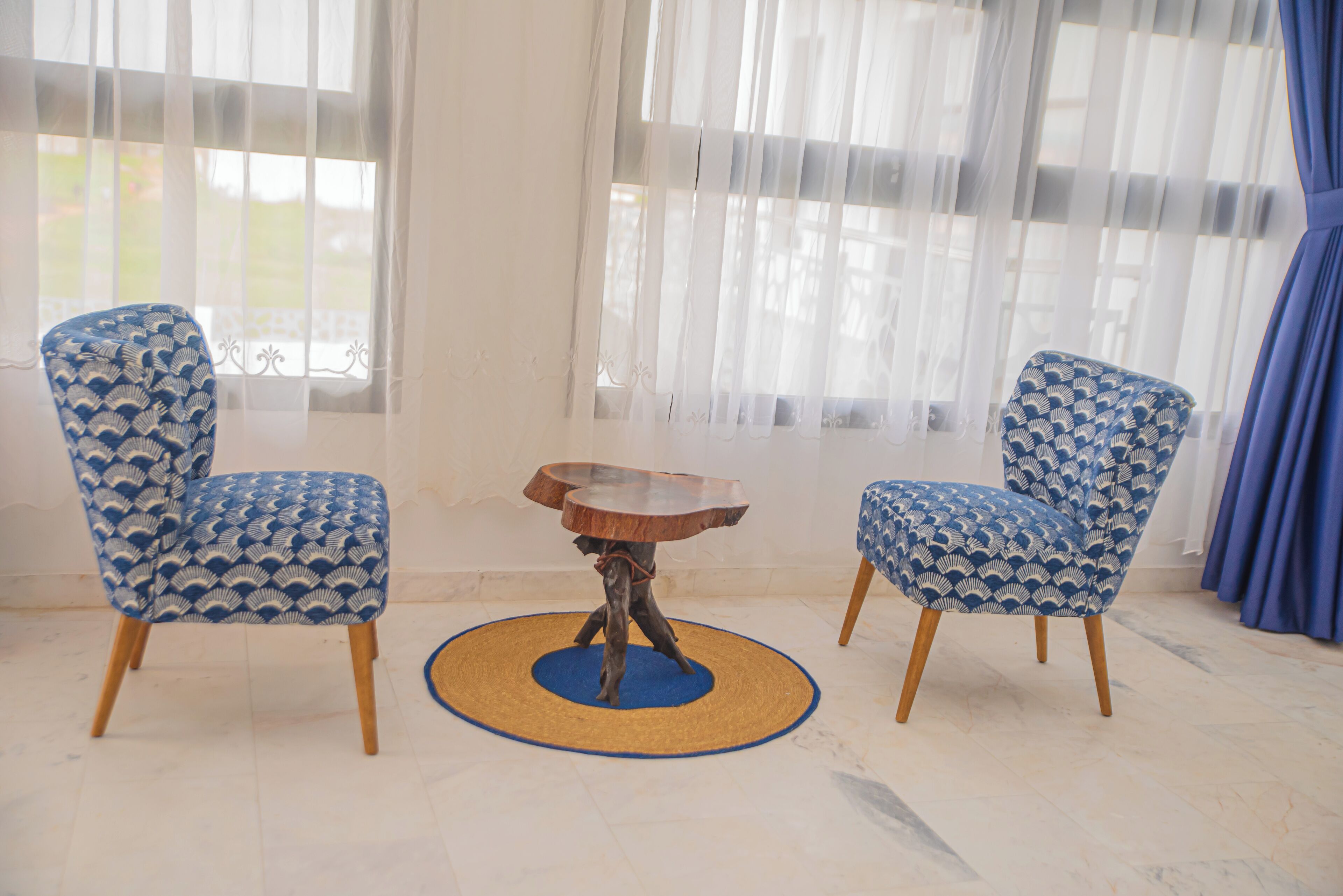 Une pièce comprenant deux fauteuils à motifs et une table ronde en bois dont le piétement est fait d’un matériau tressé.