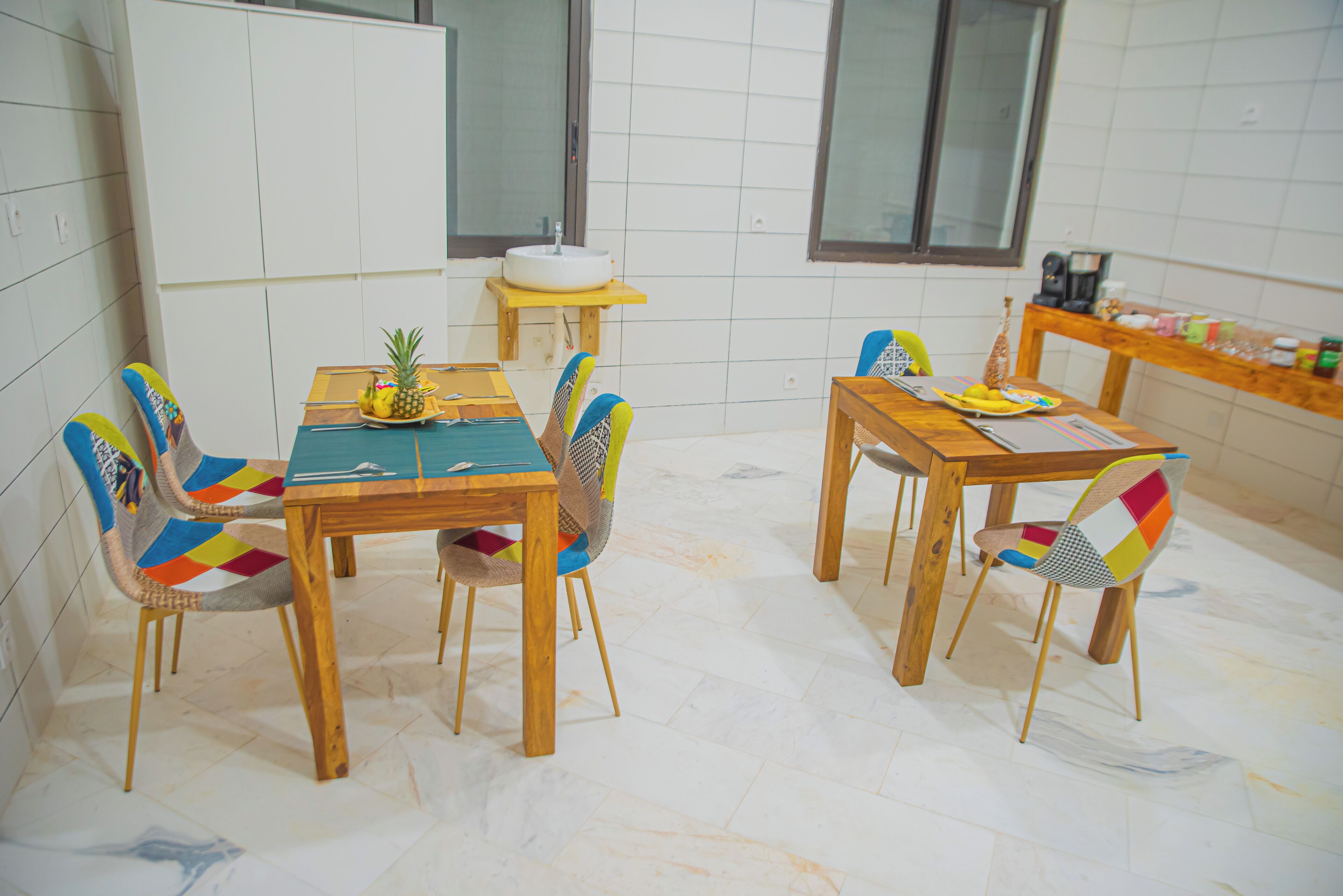 Un comedor con mesas y sillas de madera, un muro de azulejos blancos y una ventana.