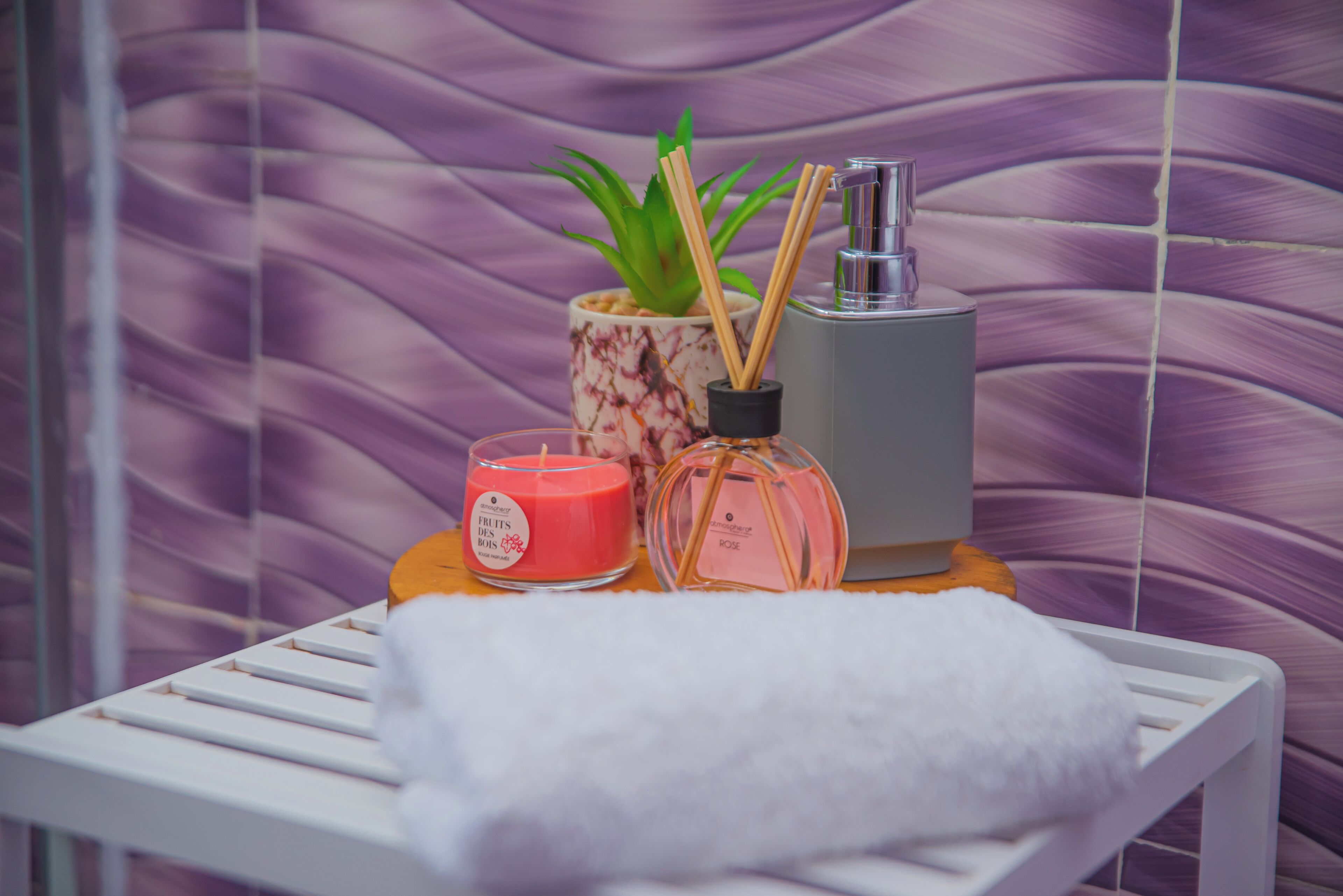 A bathroom with a white towel on a shelf, a pink candle, a glass bottle, and a potted plant.