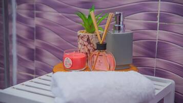A bathroom with a white towel on a shelf, a pink candle, a glass bottle, and a potted plant.
