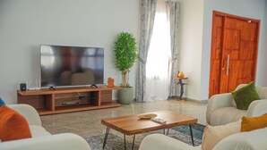 A modern living room with a flat-screen TV, a wooden coffee table, and a sofa with cushions. - La VILLA ASILI (Grand-Bassam)