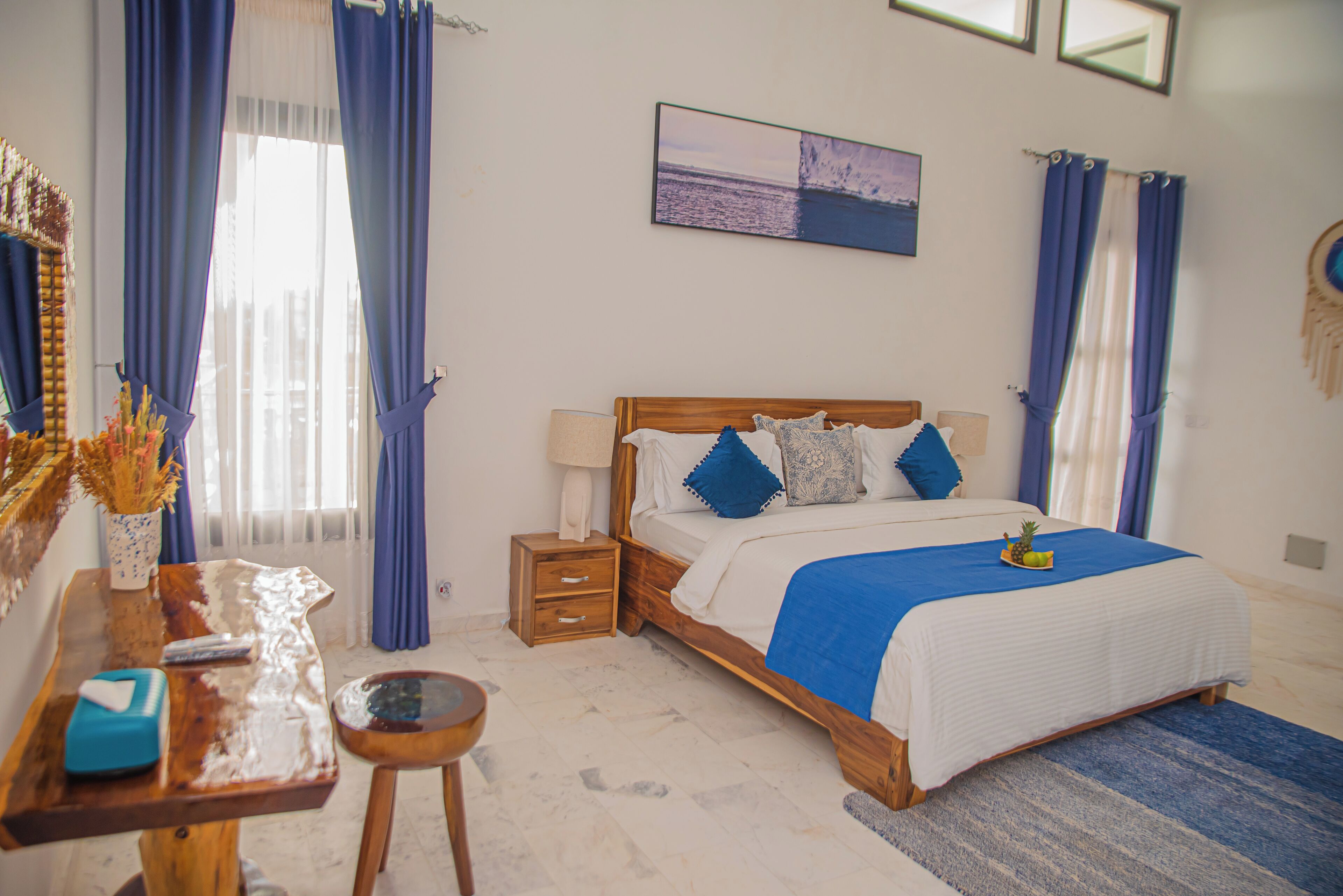 A bedroom with a wooden bed, blue bedding, a nightstand, a bedside table, and a wall-mounted painting.