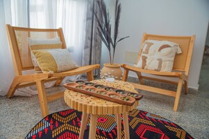 Una habitación con dos sillas de madera, una mesita con un atril decorativo y un tapete estampado.