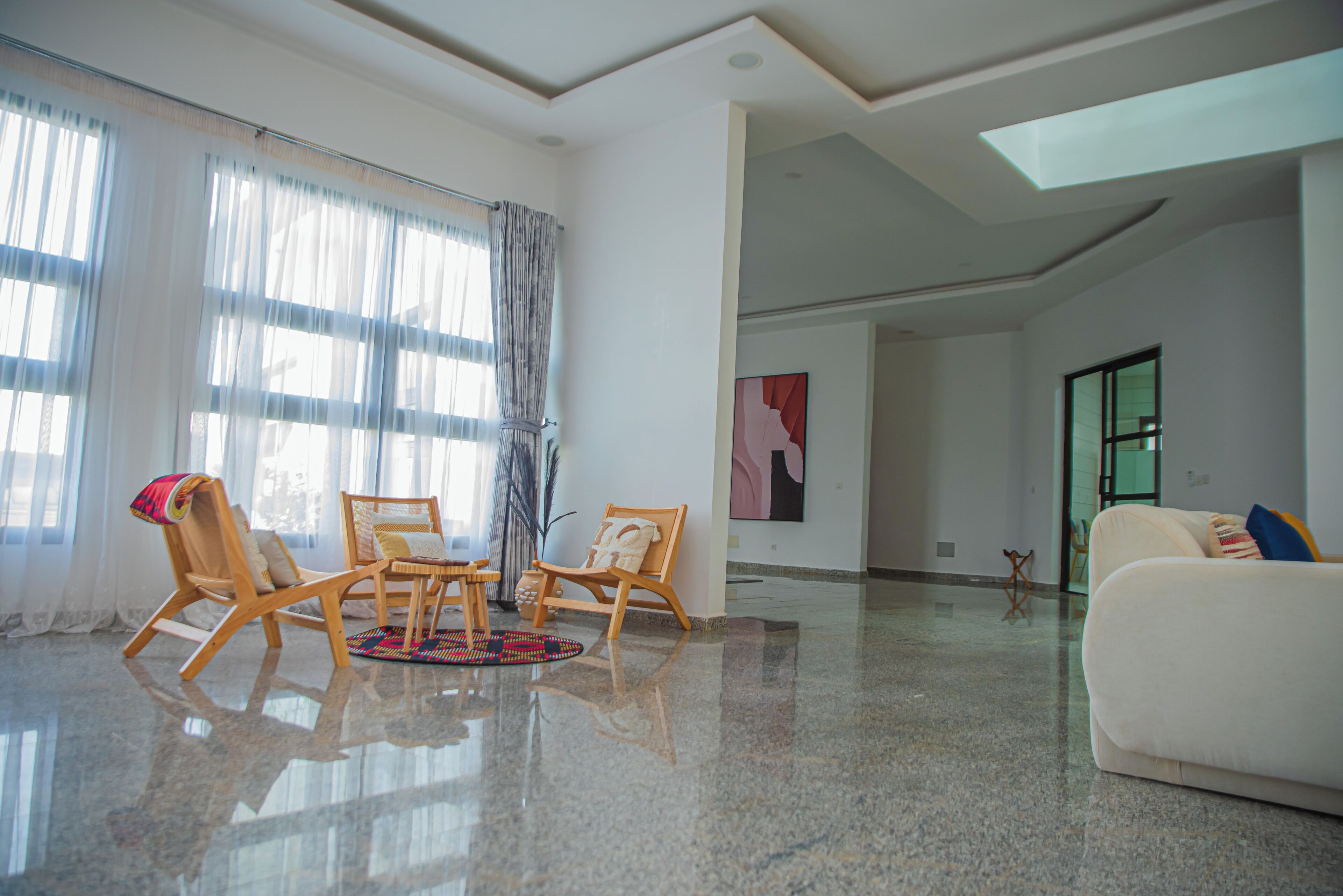 A spacious living room with a large window, a white sofa, and wooden chairs.
