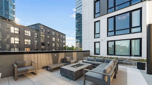 Une terrasse sur le toit, dotée d’un espace extérieur aménagé, d’un foyer et offrant une vue sur les bâtiments environnants.