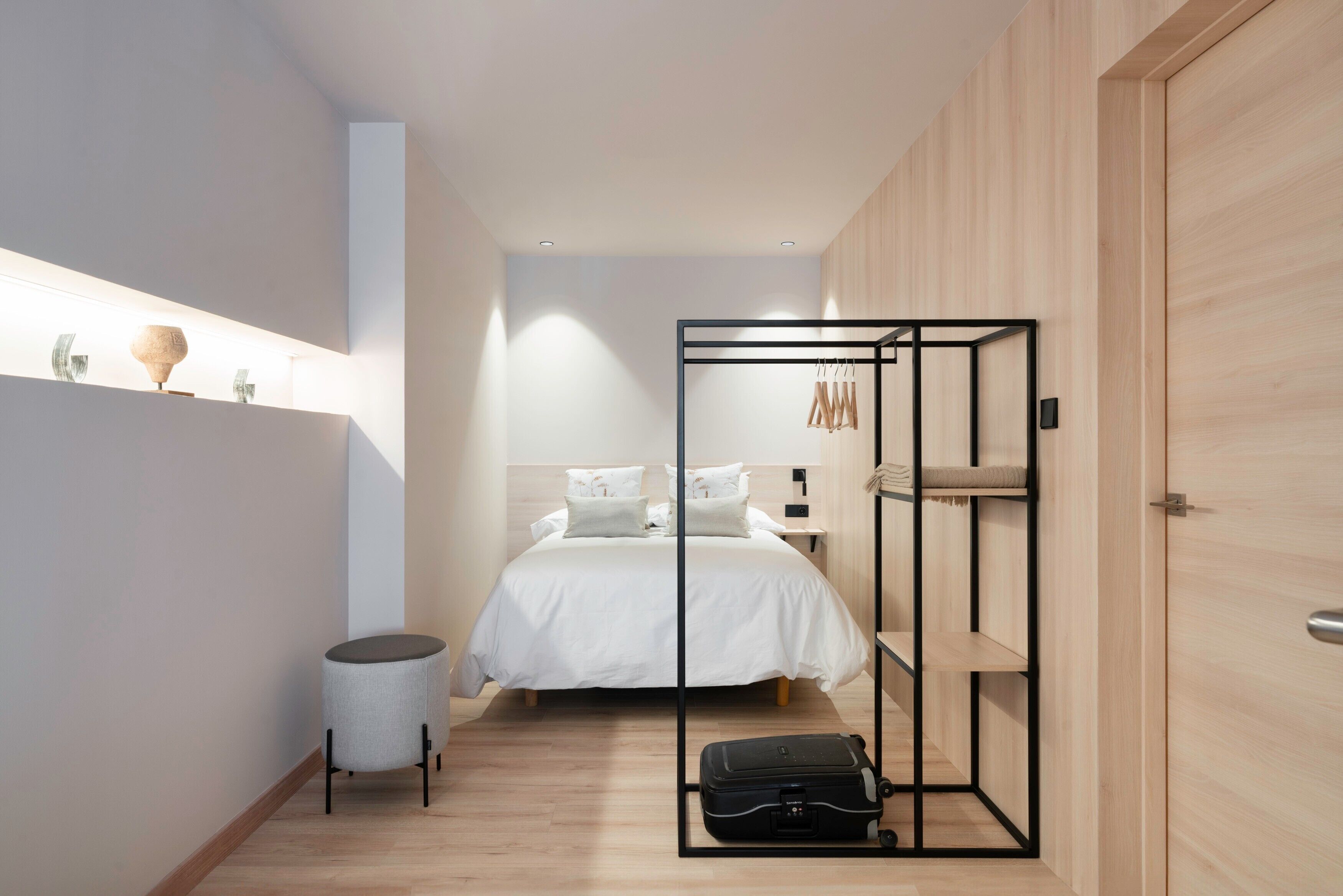 Un dormitorio moderno con cama, mesitas de noche, un armario, una pequeña mesa redonda y una maleta.