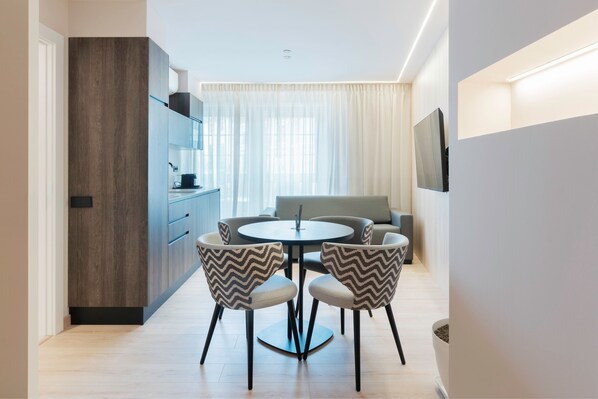 A modern dining area with a round table, two chairs, a sofa, and a TV mounted on the wall.