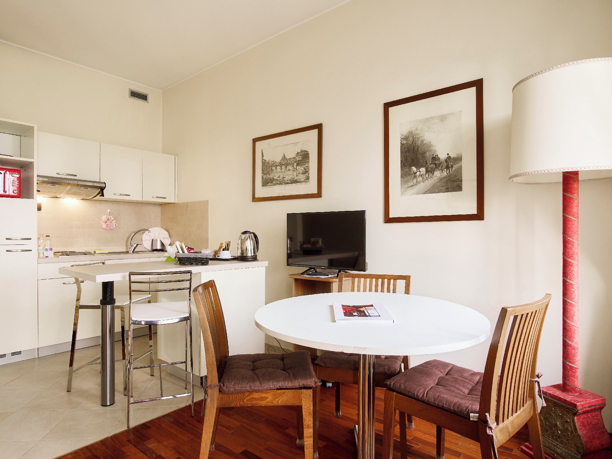 A modern kitchen with white cabinets, a dining table with four chairs, a television, and two framed pictures on the wall.