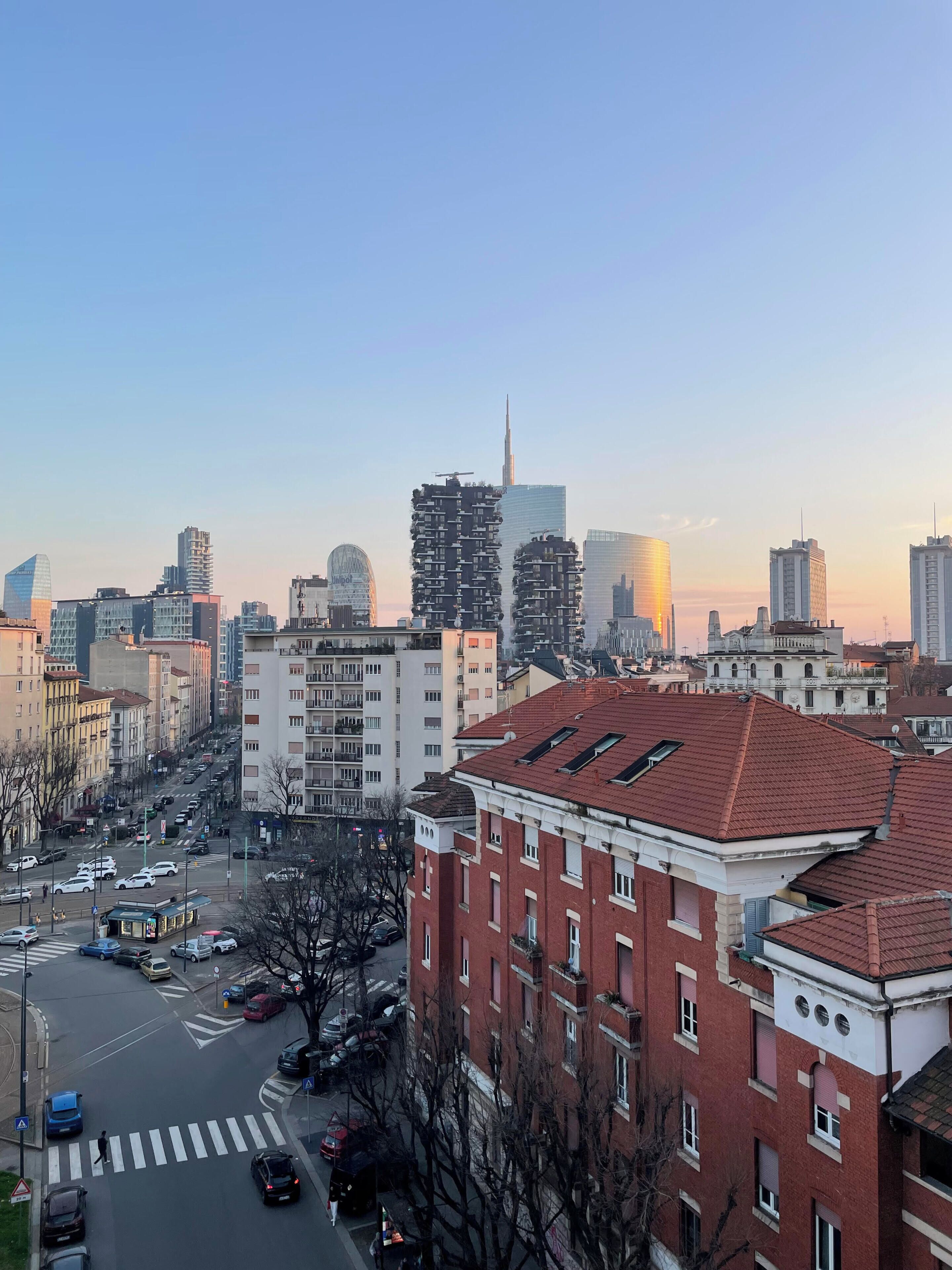 Un paisaje urbano con edificios modernos y tradicionales, cielo despejado y un paso de peatones.