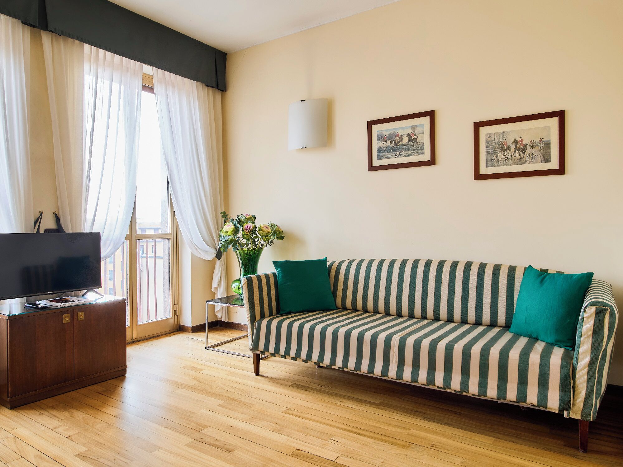 A living room with a sofa, a TV, a vase with flowers, and two framed pictures on the wall.
