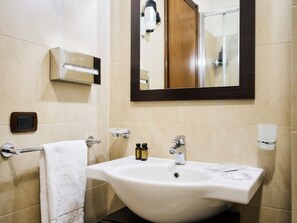 Un bagno con un lavandino bianco, un portascopino, uno specchio e una luce a parete.