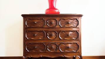 Une commode en bois avec six tiroirs, sur laquelle est posé un vase rouge.