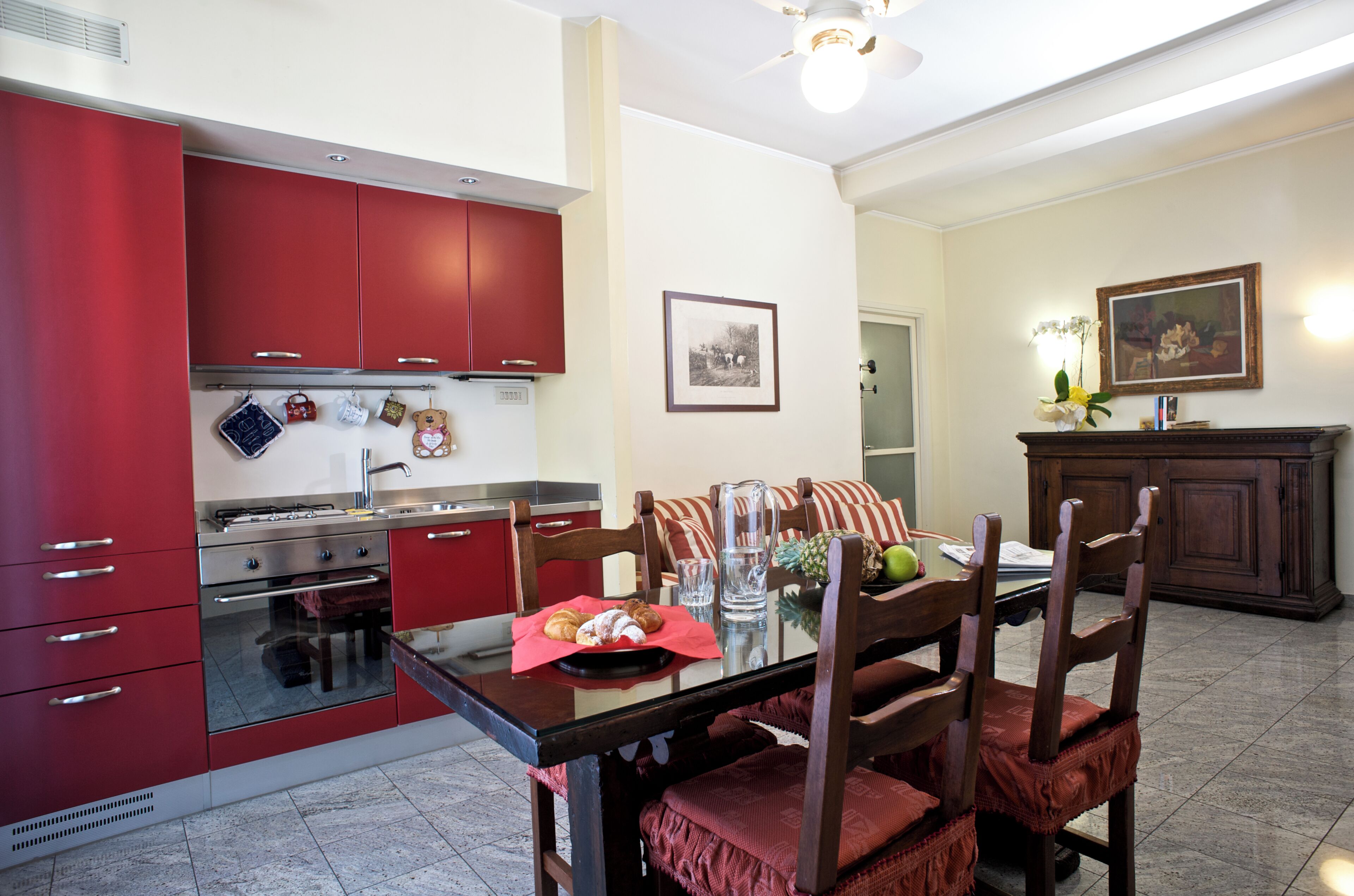 Uma cozinha com armários vermelhos, uma mesa de jantar com cadeiras e um quadro na parede.