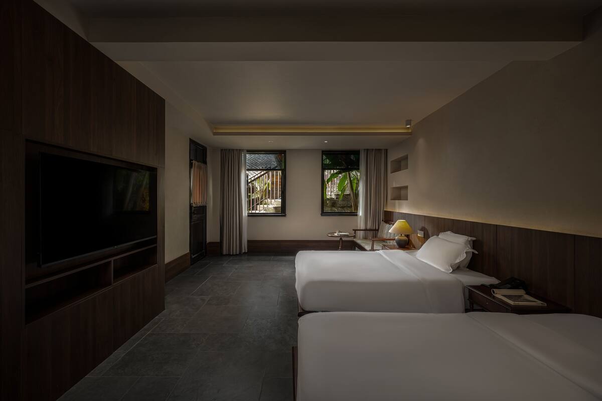 Ein Hotelzimmer mit zwei Betten, einem Fernseher, einem kleinen Tisch und einem Fenster mit Vorhängen.