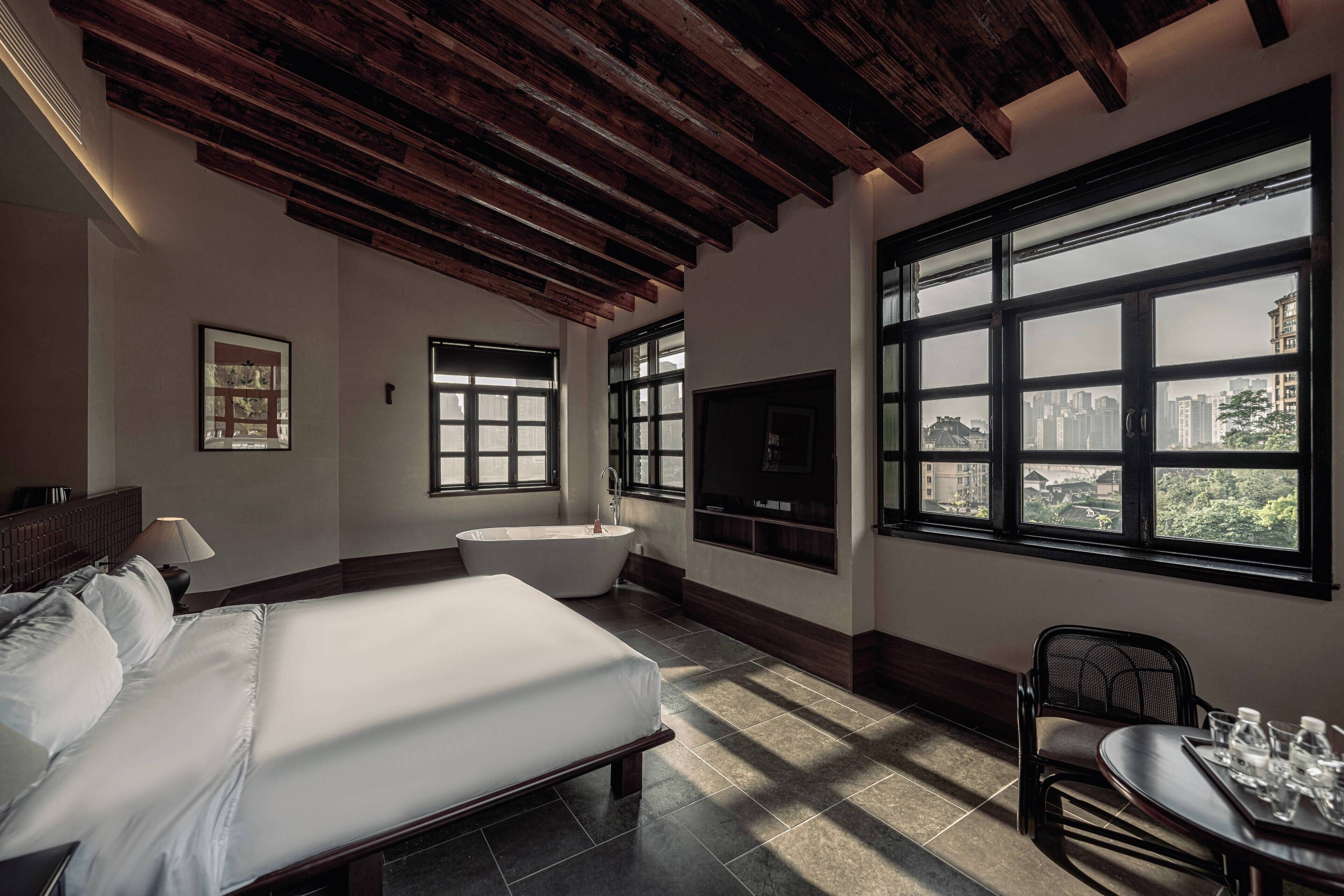A hotel room with a large bed, a bathtub, a dining table with chairs, and a TV.