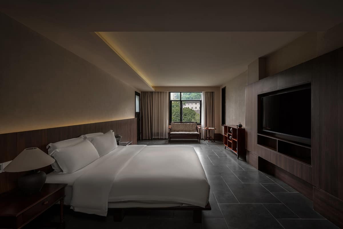 Ein modernes Hotelzimmer mit einem großen Bett, einem Fernseher und Blick auf Grünflächen.