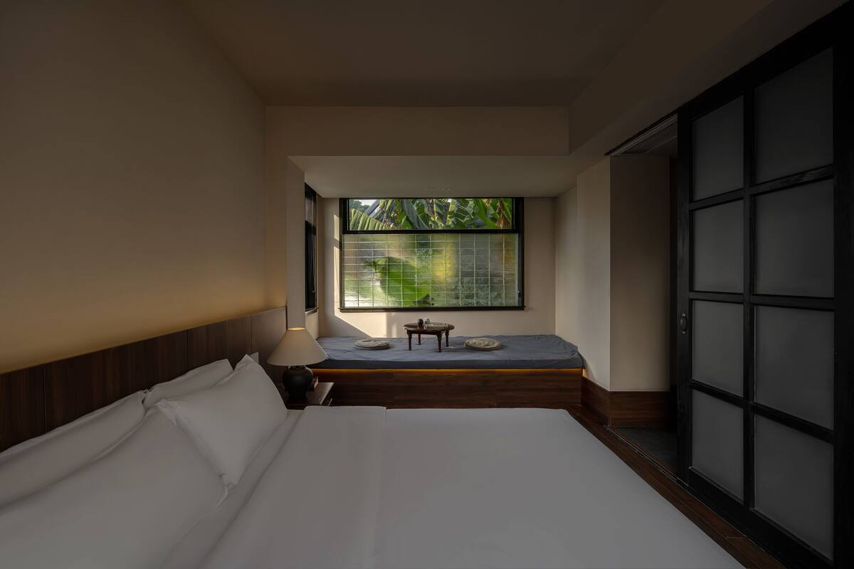 Ein Zimmer mit einem Bett, einem kleinen Tisch mit Stuhl, einem Fenster mit Blick ins Grüne und Schiebetüren.