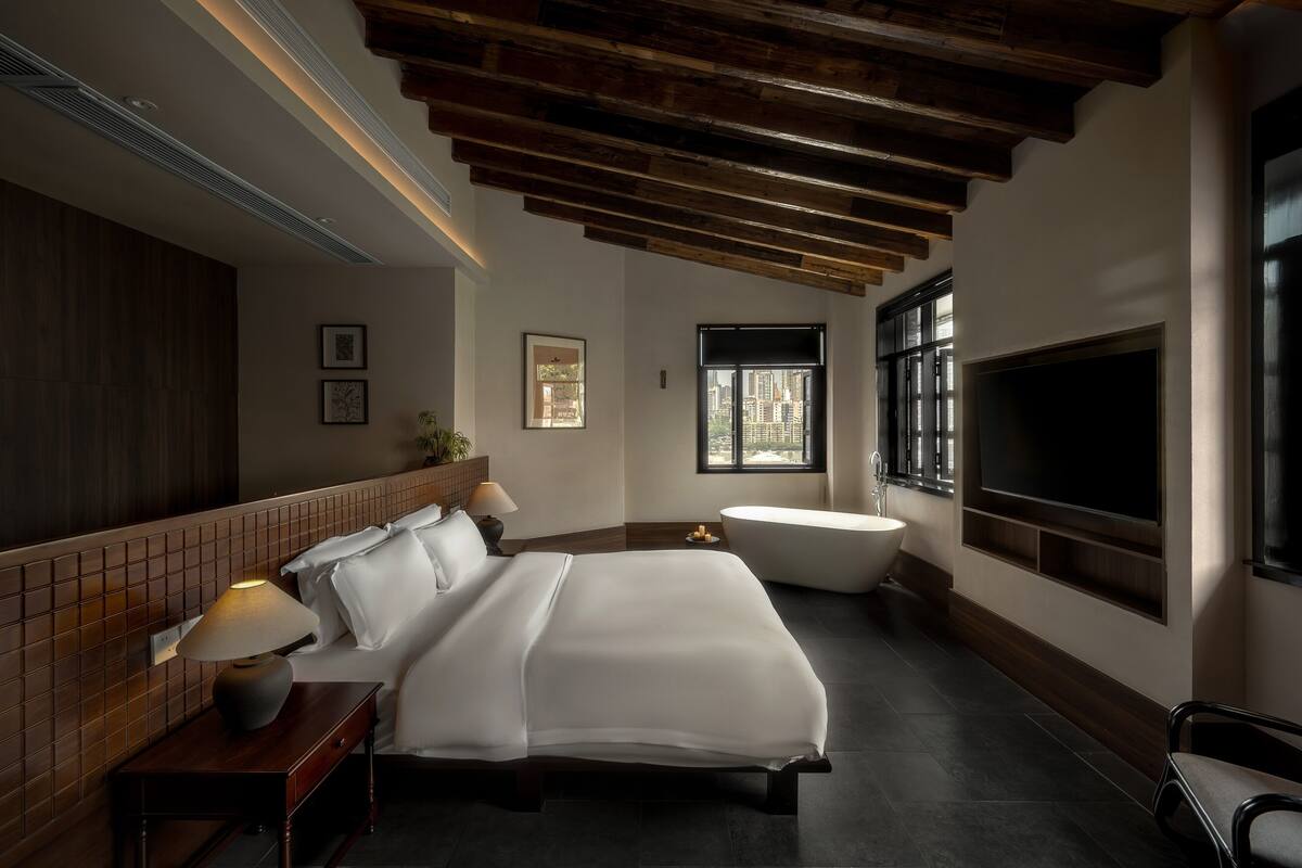 Ein modernes Hotelzimmer mit einem großen Bett, einer Badewanne, einem Fernseher und einem Fenster mit Blick auf die Stadt.
