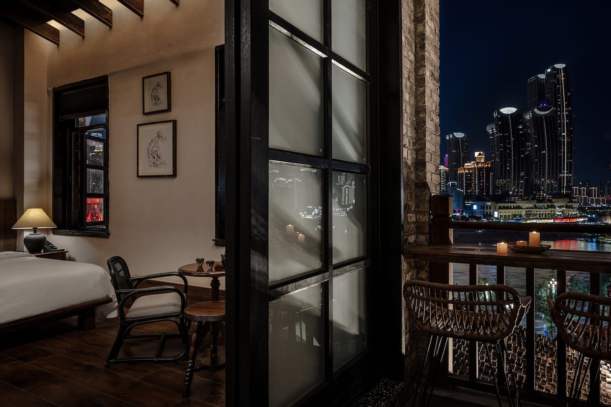 Ein Hotelzimmer mit Bett, Schreibtisch, Stuhl und Blick auf eine nächtliche Stadtlandschaft.