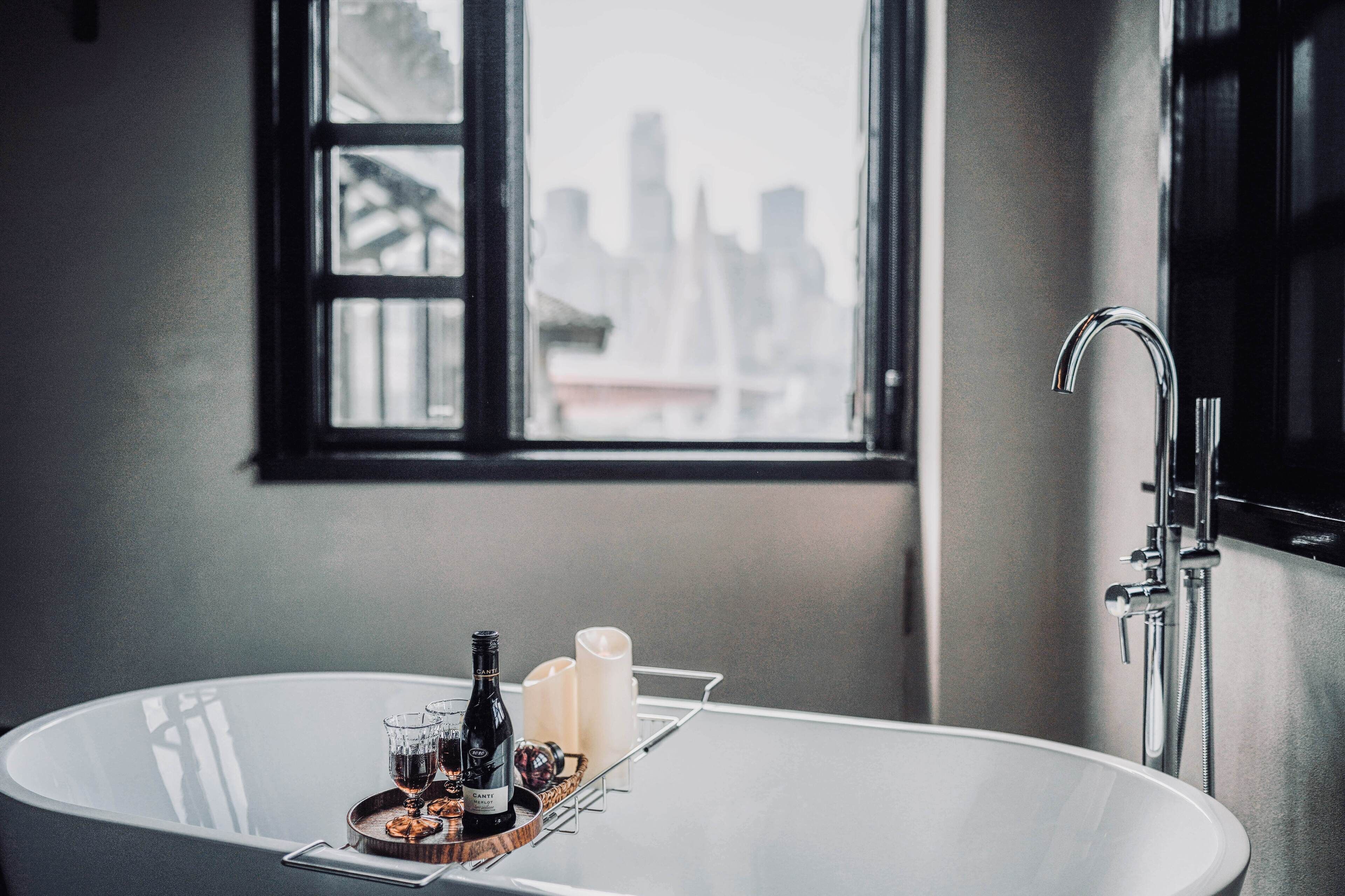 Un baño con bañera, una ventana con vista a la ciudad y una bandeja con botellas y velas.