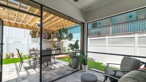 Eine moderne Terrasse mit Glastür, Gartenmöbeln, einer Holz-Pergola und Blick auf einen umzäunten Garten.