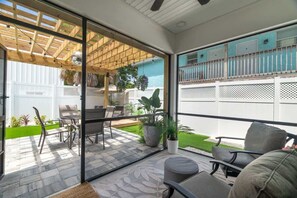 Eine moderne Terrasse mit Glastür, Gartenmöbeln, einer Holz-Pergola und Blick auf einen umzäunten Garten.